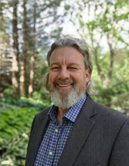 Portrait photograph of Ed VanderWindt standing outdoors in front of a forest